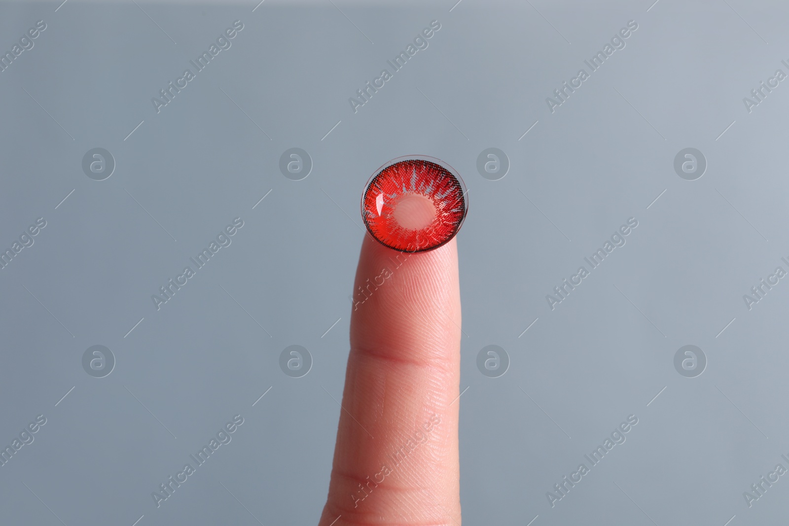 Photo of Woman holding color contact lens on light grey background, closeup