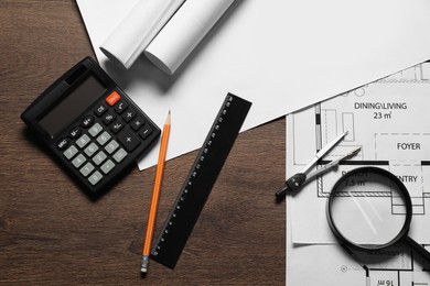 Photo of Different architectural drawings, pencil, magnifying glass, ruler, calculator and dividers on wooden table, flat lay