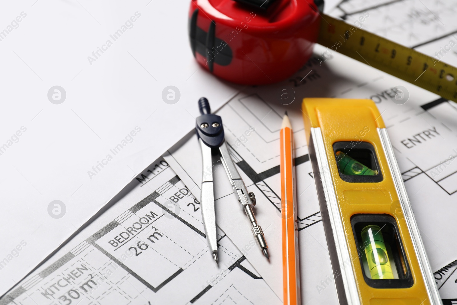 Photo of Pencil, dividers, building level and measuring tape on different architectural drawings, closeup