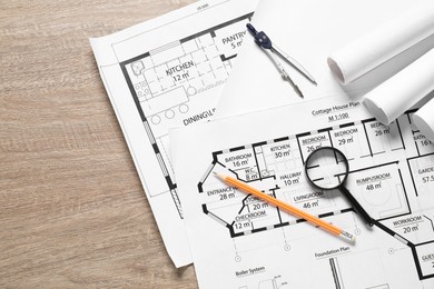 Different engineering drawings, dividers, pencil and magnifying glass on wooden table, top view