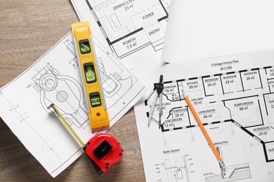 Photo of Different engineering drawings, building level, measuring tape, pencil and dividers on wooden table, flat lay