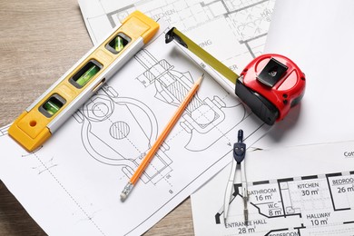 Photo of Different engineering drawings, building level, measuring tape, pencil and dividers on wooden table, above view