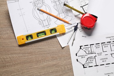 Different engineering drawings, building level, measuring tape, pencil and dividers on wooden table, flat lay