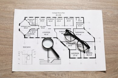 Different engineering drawings, glasses and magnifying glass on wooden table, top view