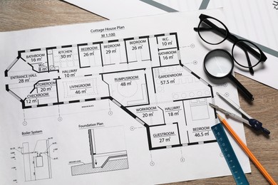 Photo of Different engineering drawings, pencil, dividers, ruler, glasses and magnifying glass on wooden table, flat lay