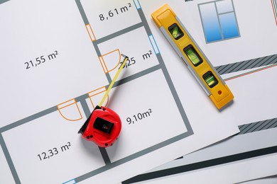 Photo of Building level and measuring tape on architectural drawings, flat lay