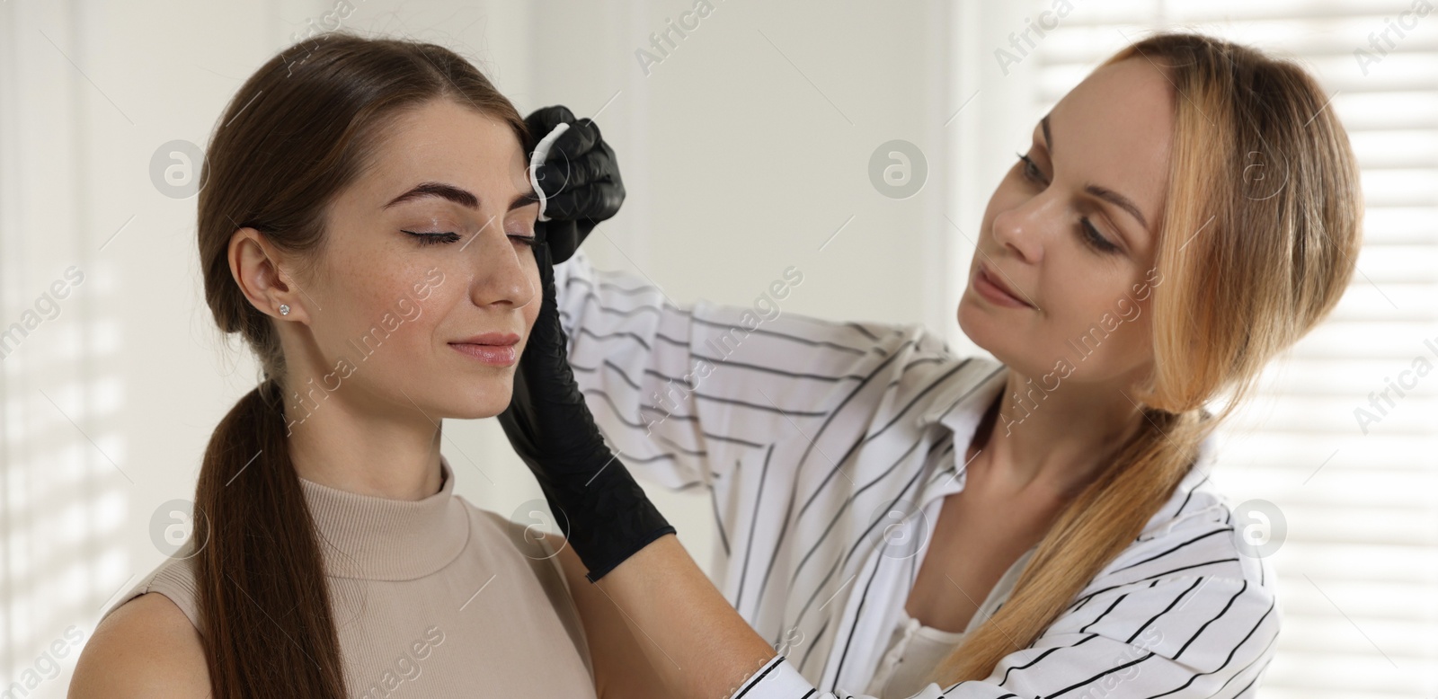 Photo of Beautician wiping client`s eyebrows after henna dyeing in salon