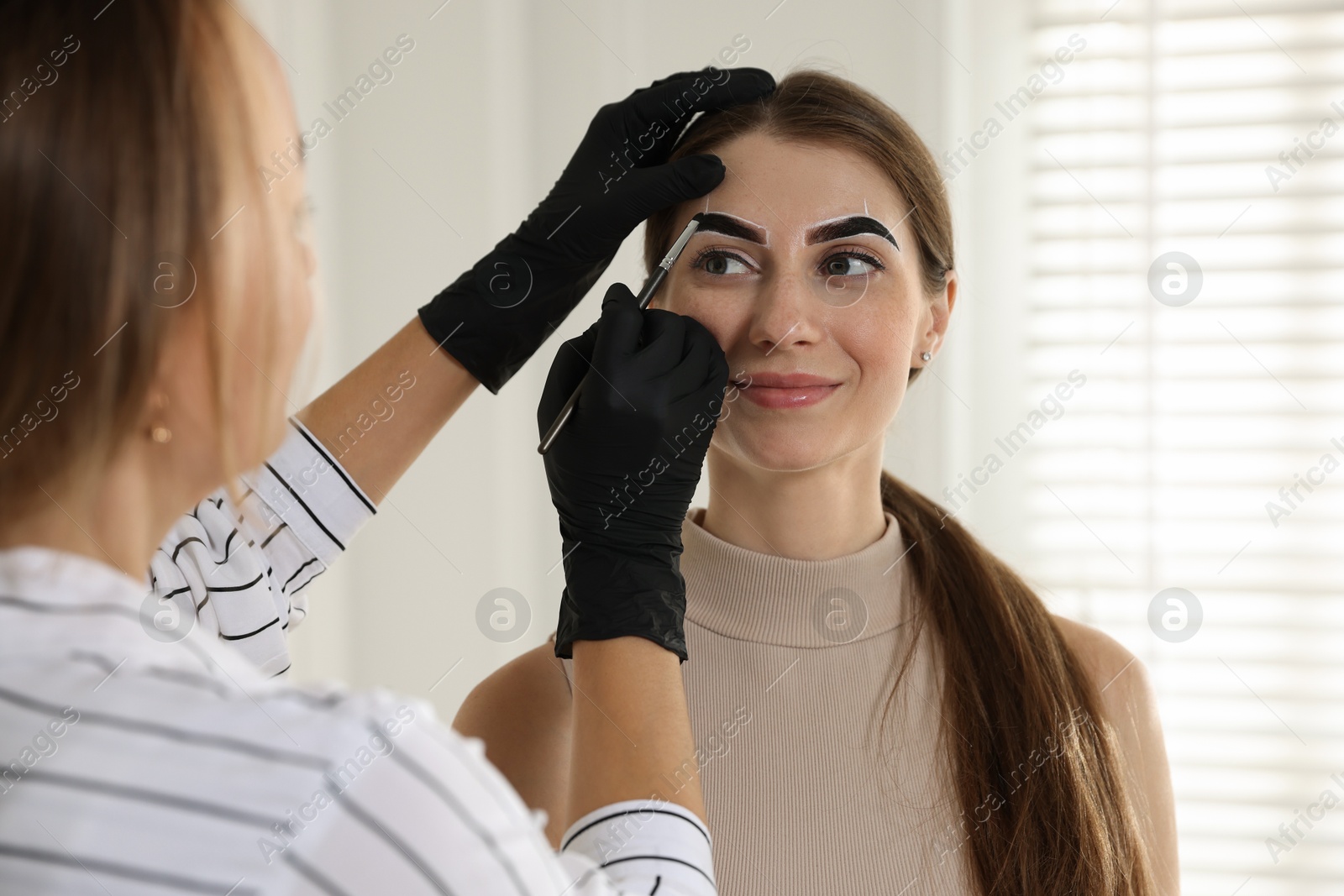 Photo of Beautician dyeing client’s eyebrows with henna in salon, closeup