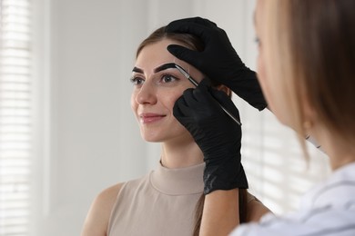 Photo of Beautician dyeing client’s eyebrows with henna in salon, closeup