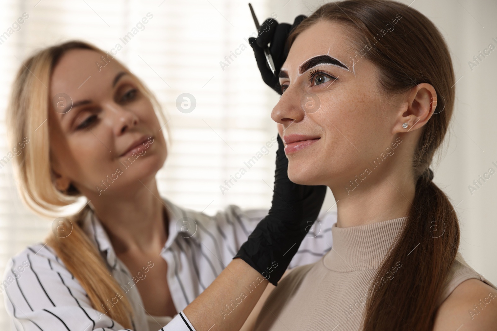 Photo of Beautician dyeing client’s eyebrows with henna in salon, selective focus