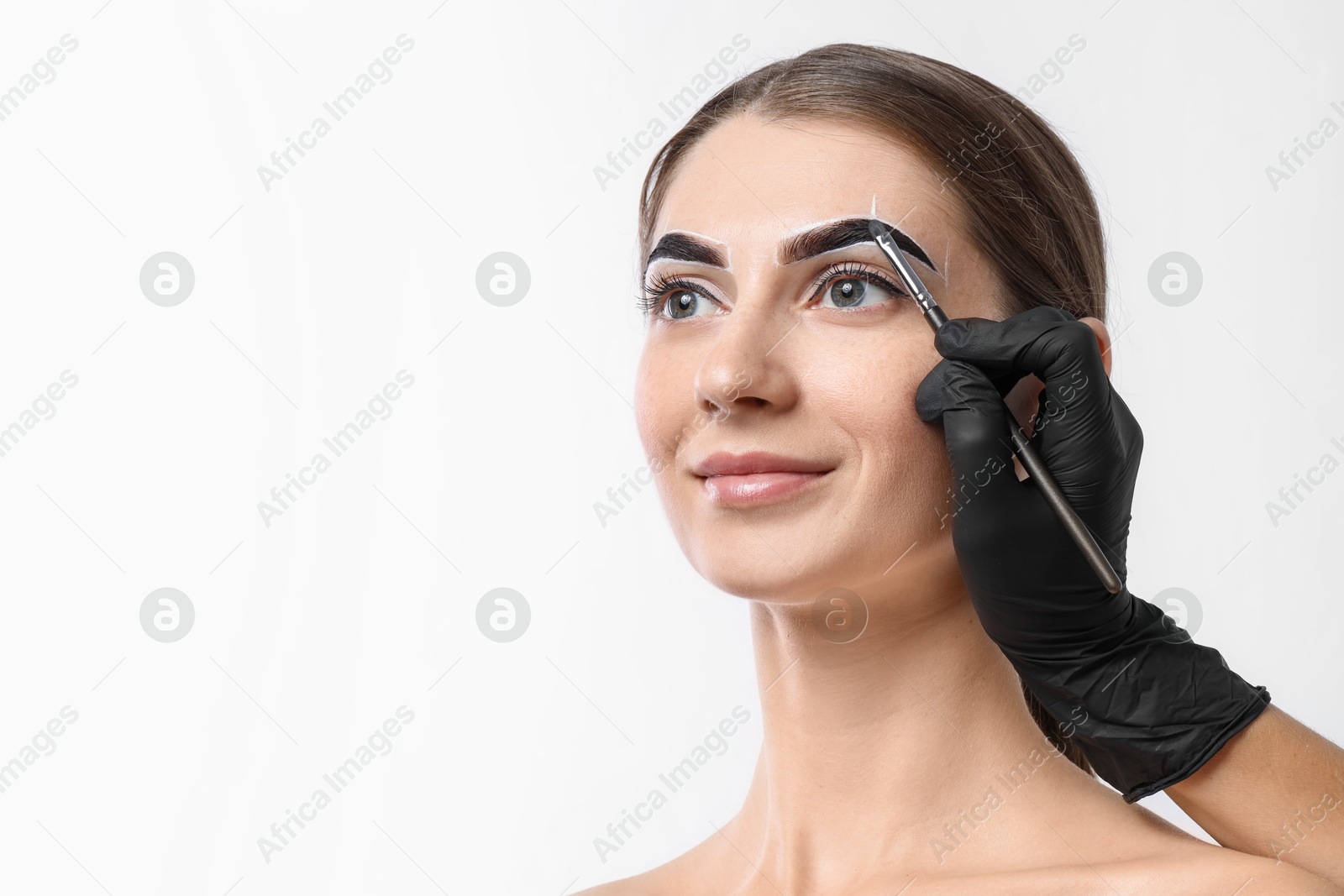 Photo of Young woman undergoing henna eyebrows dyeing on light background, closeup. Space for text