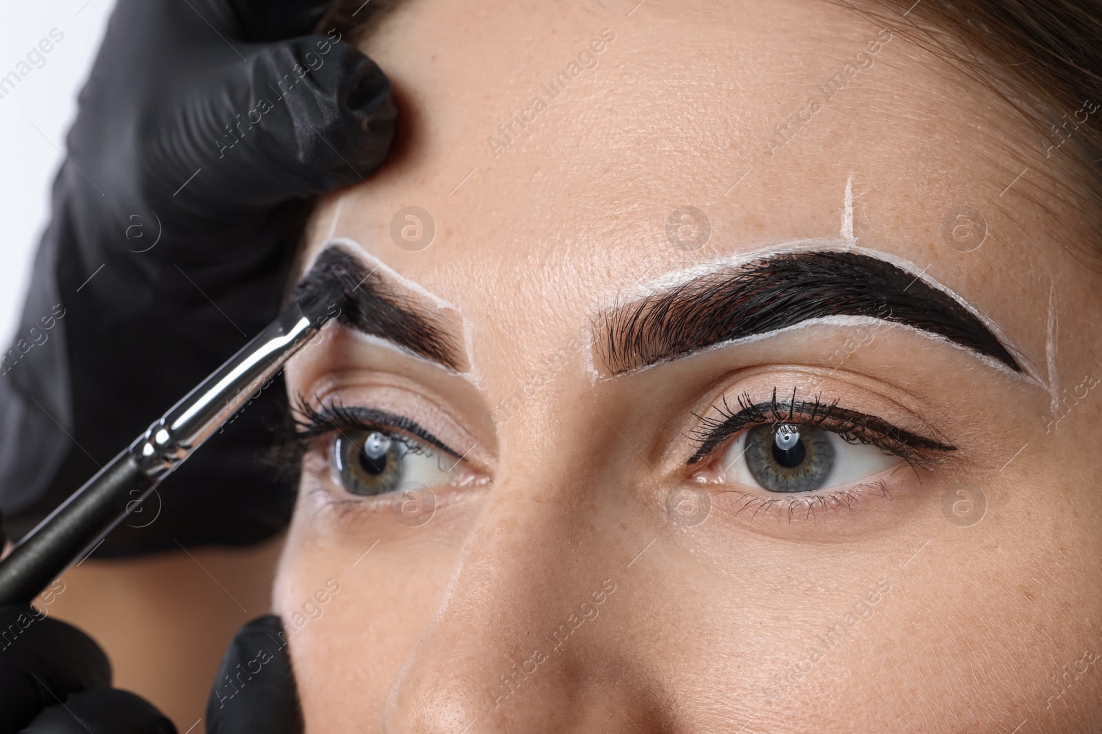 Photo of Young woman undergoing henna eyebrows dyeing on light background, closeup