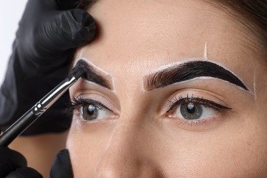 Young woman undergoing henna eyebrows dyeing on light background, closeup