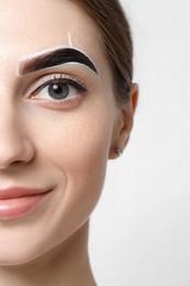 Young woman during henna eyebrows dyeing procedure on light background, closeup