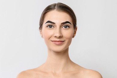 Beautiful young woman during henna eyebrows dyeing procedure on light background