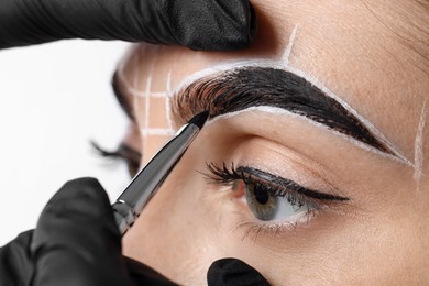 Photo of Young woman undergoing henna eyebrows dyeing procedure on light background, closeup