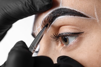 Photo of Young woman undergoing henna eyebrows dyeing procedure on light background, closeup