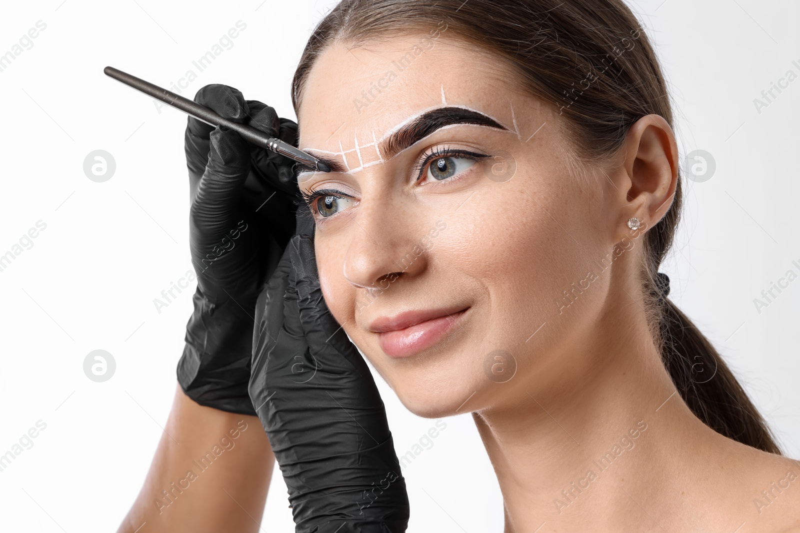 Photo of Young woman undergoing henna eyebrows dyeing procedure on light background, closeup