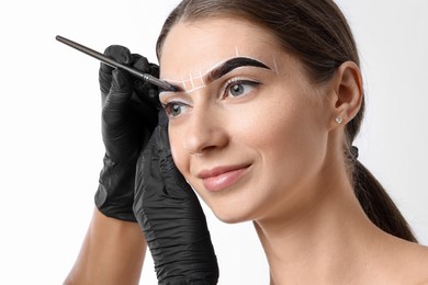 Young woman undergoing henna eyebrows dyeing procedure on light background, closeup