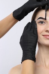 Young woman undergoing henna eyebrows dyeing procedure on light background, closeup