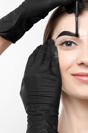 Young woman undergoing henna eyebrows dyeing procedure on light background, closeup