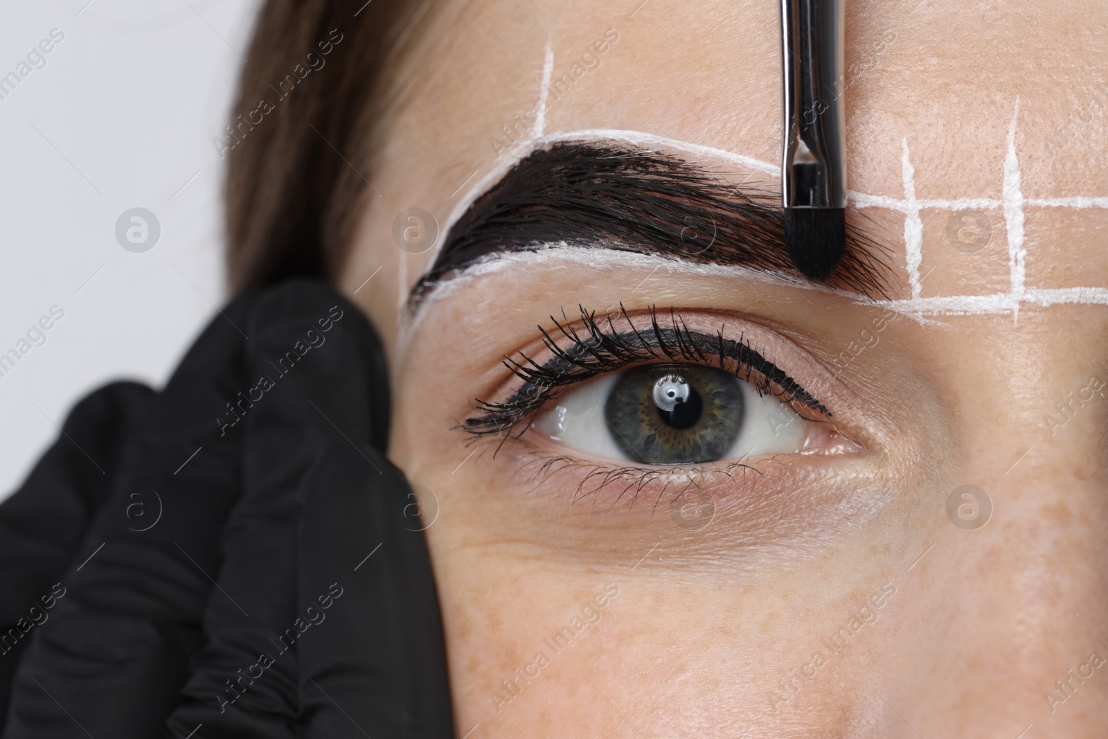 Photo of Young woman undergoing henna eyebrows dyeing procedure on light background, closeup