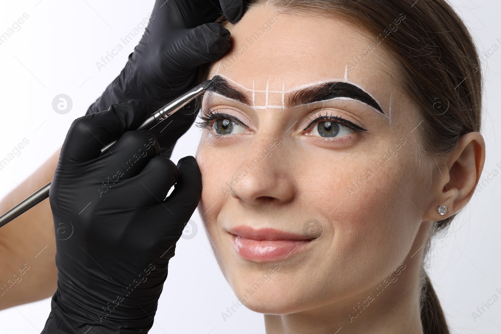 Photo of Young woman undergoing henna eyebrows dyeing procedure on light background, closeup