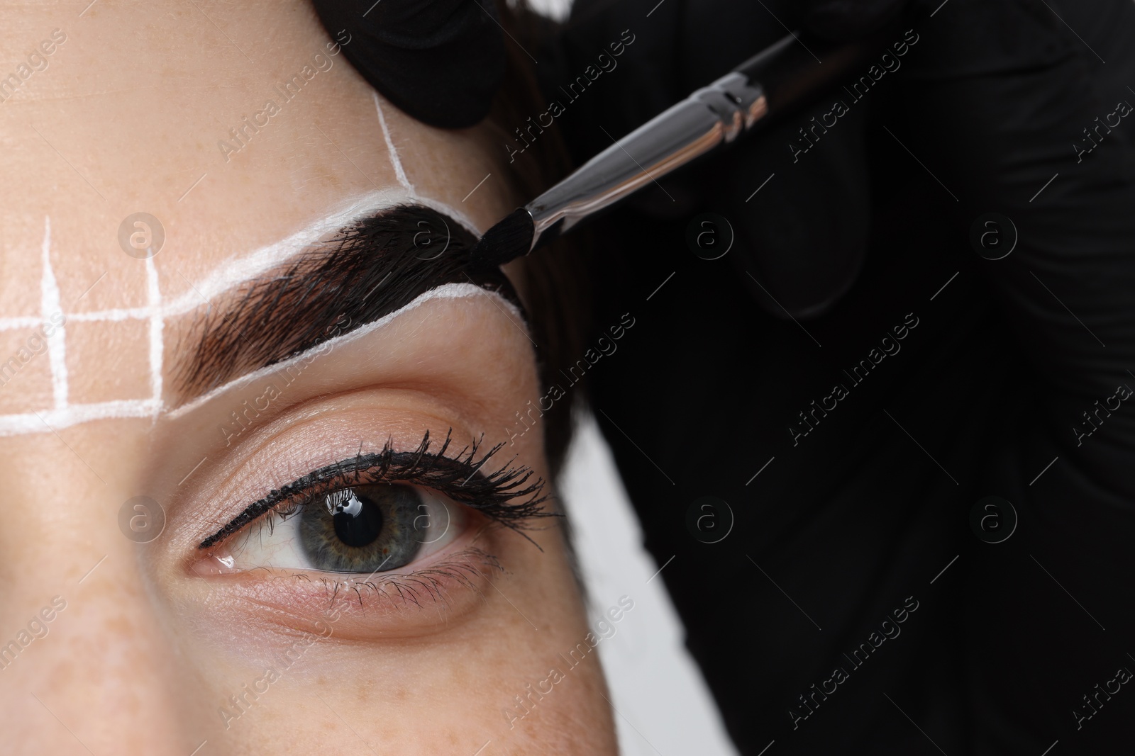 Photo of Young woman undergoing henna eyebrows dyeing procedure, closeup