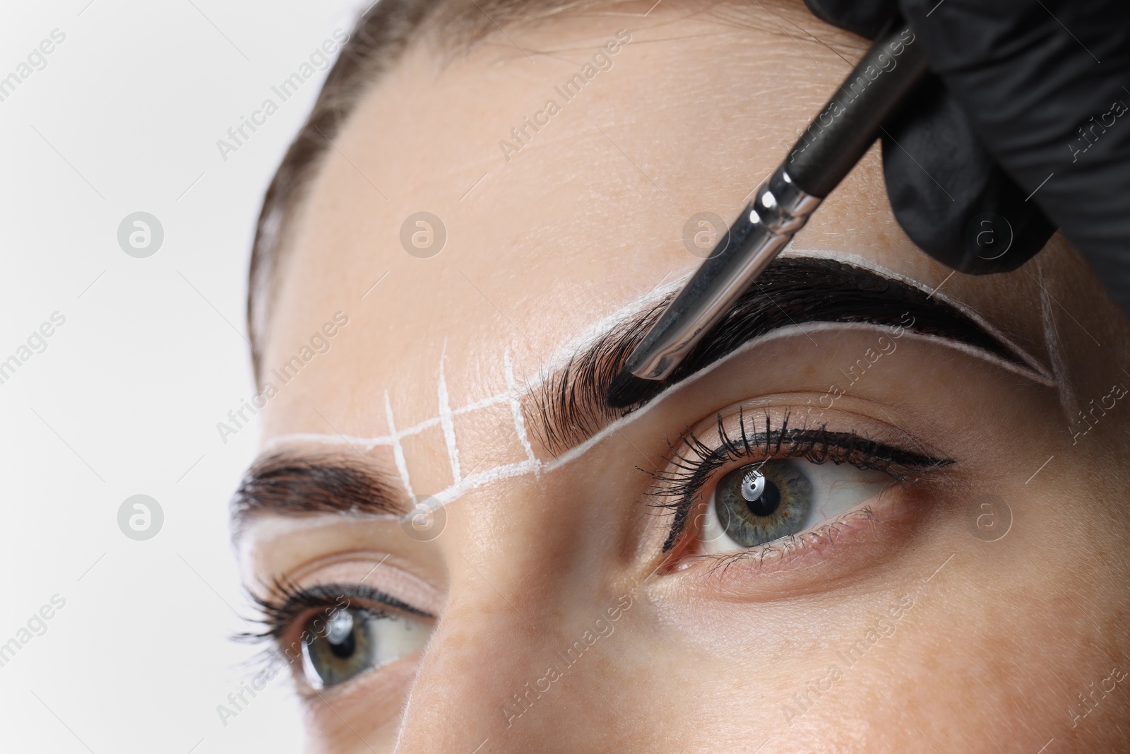 Photo of Young woman undergoing henna eyebrows dyeing on light background, closeup