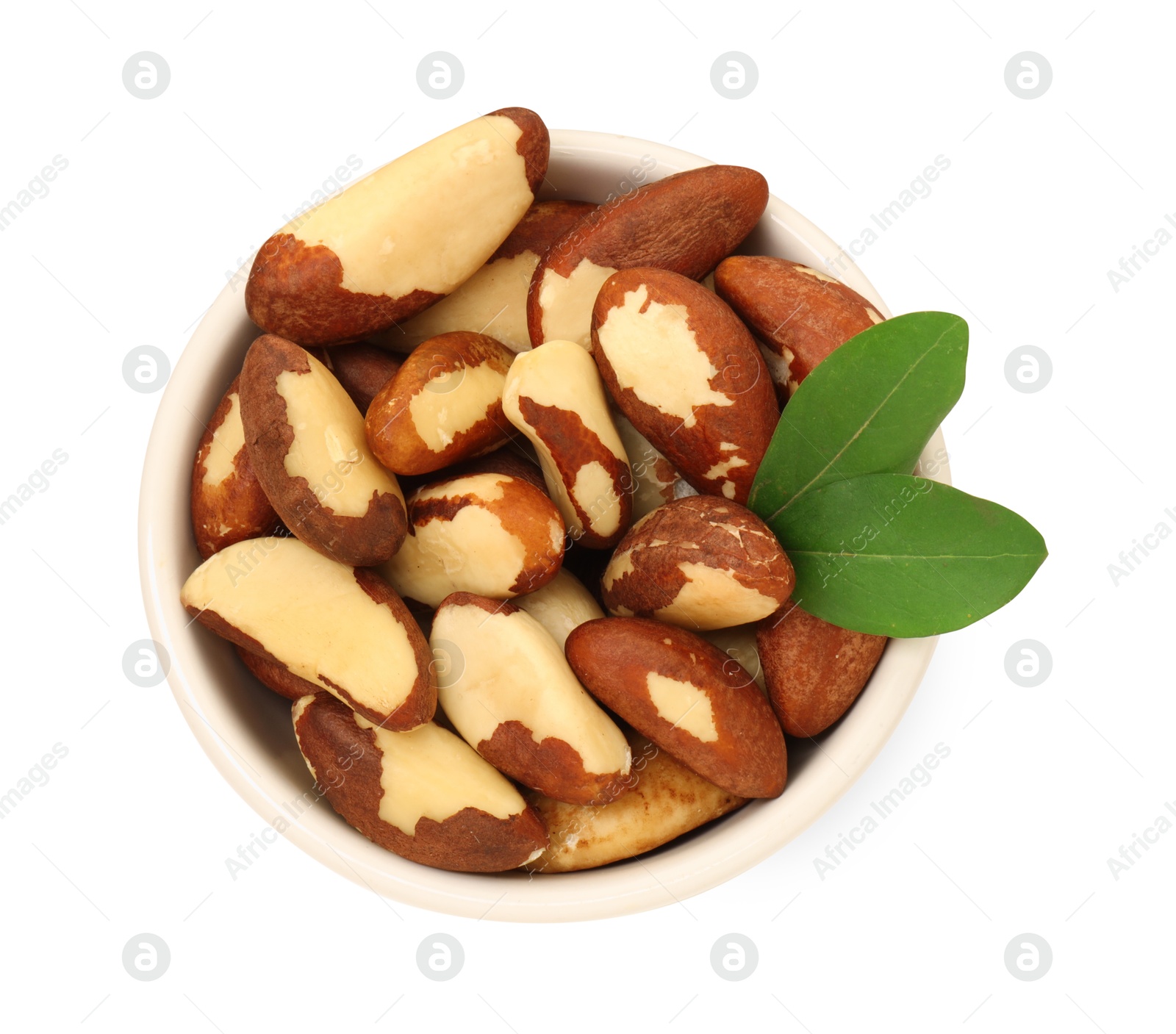 Photo of Tasty Brazil nuts and green leaves in bowl isolated on white, top view