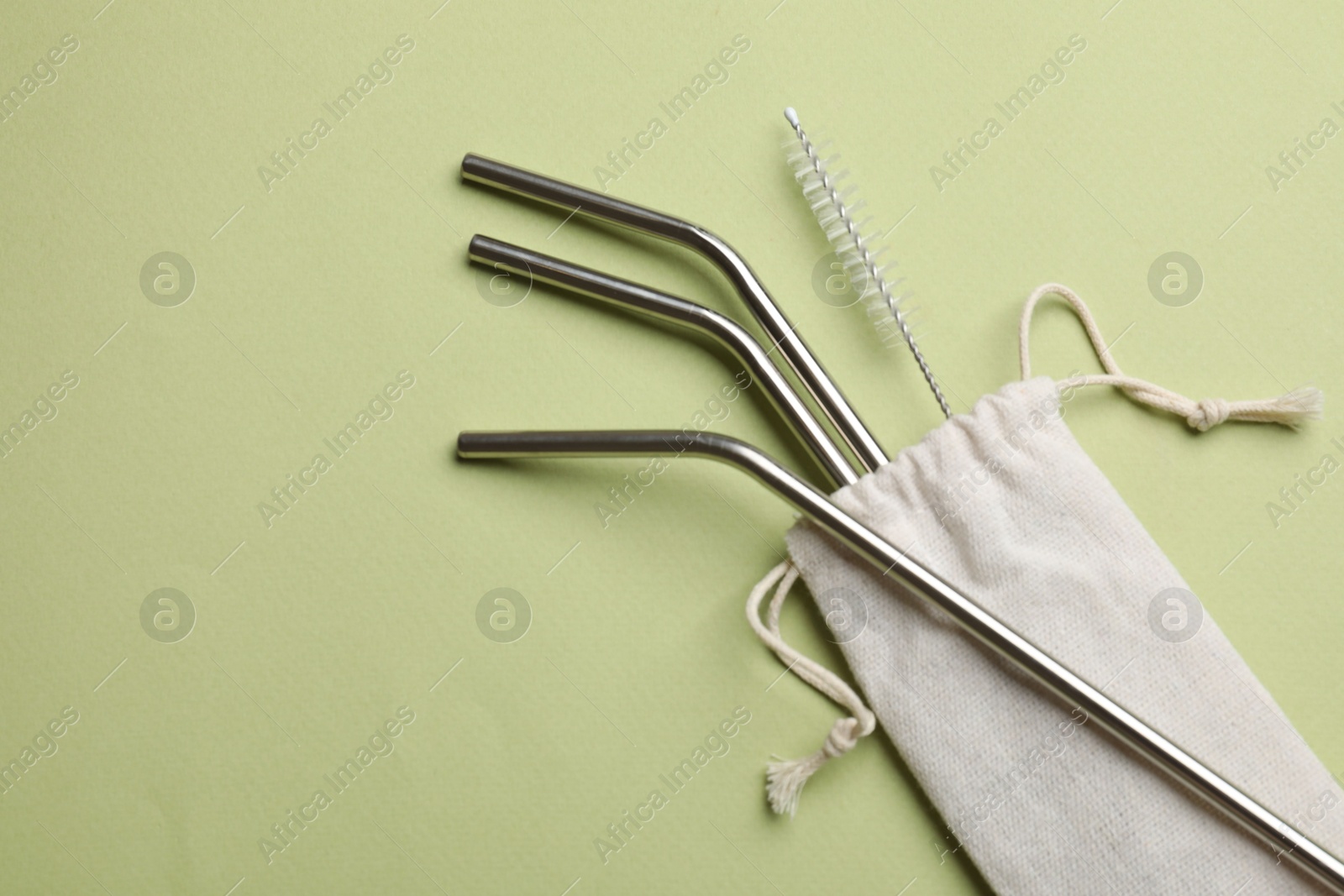 Photo of Metal drinking straws and cleaning brush on green background, top view. Space for text