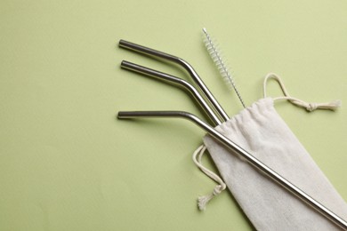 Photo of Metal drinking straws and cleaning brush on green background, top view. Space for text