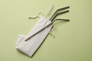 Photo of Metal drinking straws and cleaning brush on green background, top view