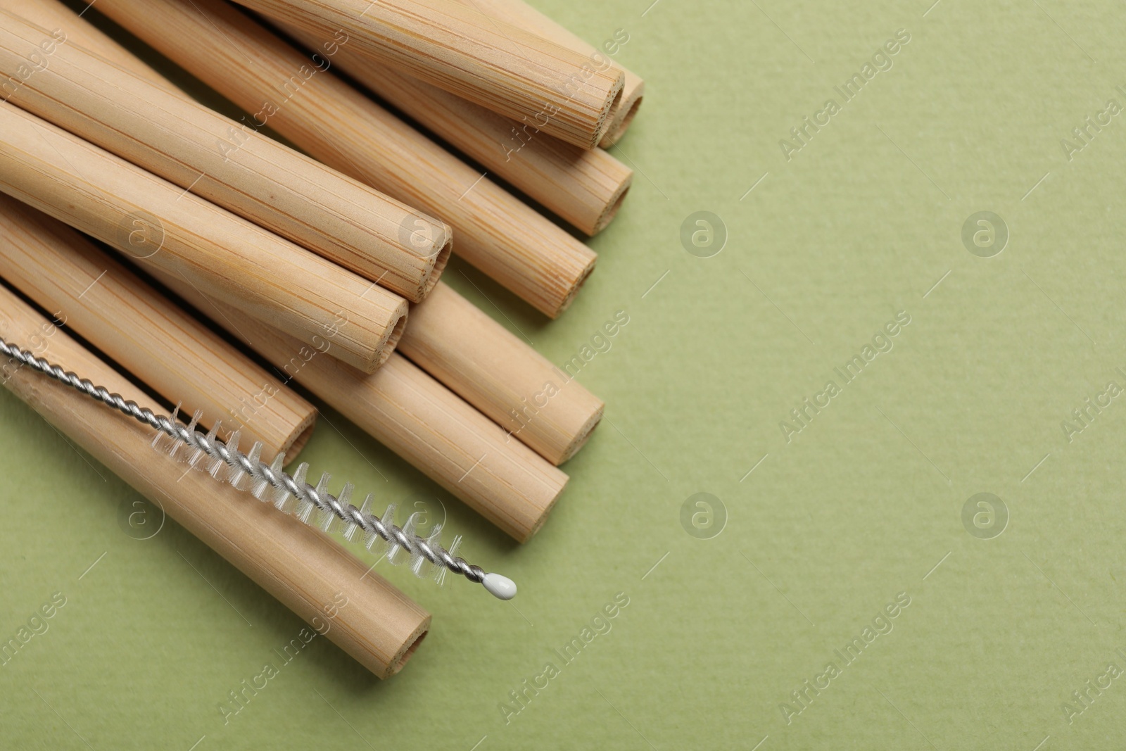 Photo of Bamboo drinking straws and cleaning brush on green background, top view. Space for text