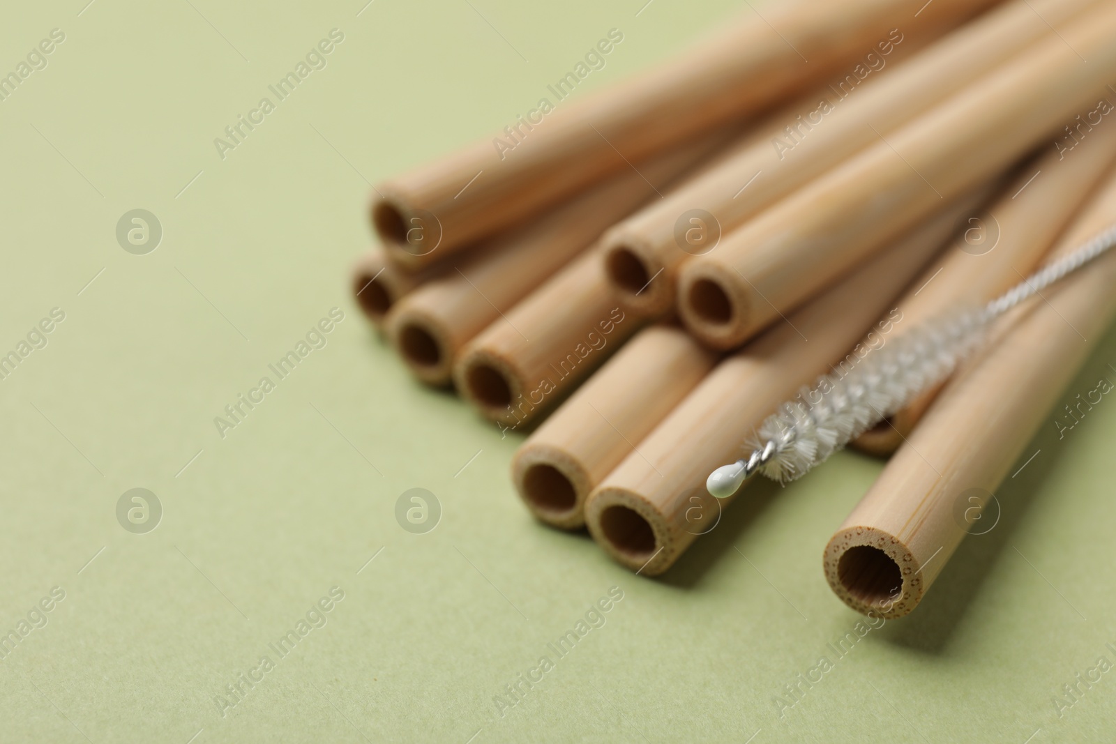 Photo of Bamboo drinking straws and cleaning brush on green background, closeup. Space for text