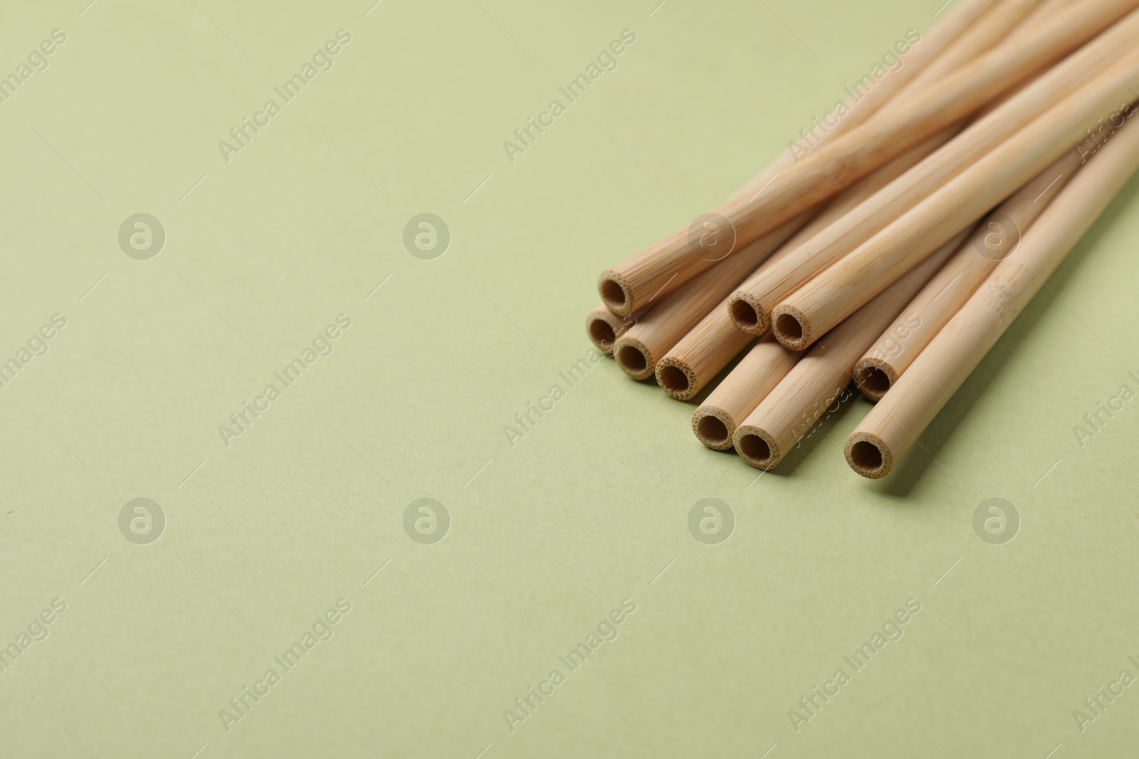 Photo of Bamboo drinking straws on green background, closeup. Space for text