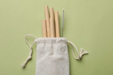 Photo of Bamboo drinking straws and cleaning brush in bag on green background, top view