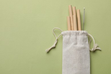 Photo of Bamboo drinking straws and cleaning brush in bag on green background, top view. Space for text