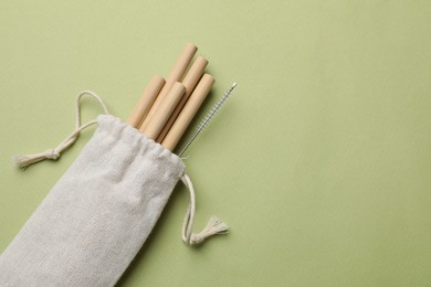 Photo of Bamboo drinking straws and cleaning brush in bag on green background, top view. Space for text