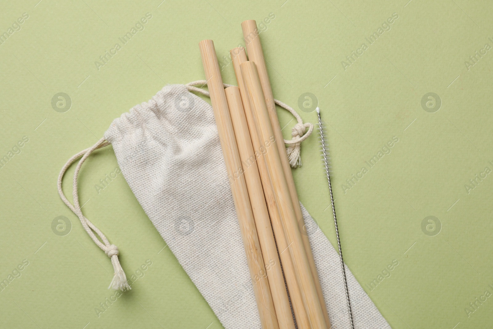 Photo of Bamboo drinking straws and cleaning brush on green background, top view