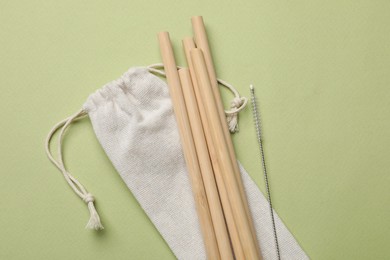 Photo of Bamboo drinking straws and cleaning brush on green background, top view