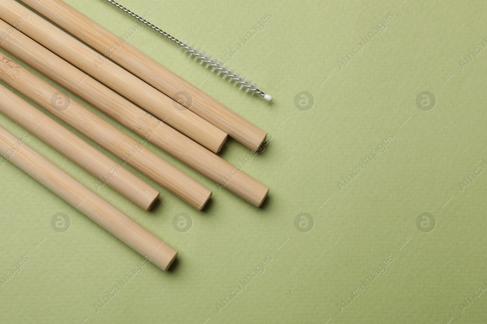 Photo of Bamboo drinking straws and cleaning brush on green background, top view. Space for text