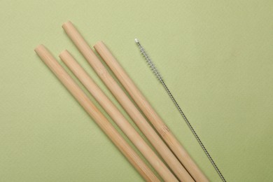 Photo of Bamboo drinking straws and cleaning brush on green background, top view