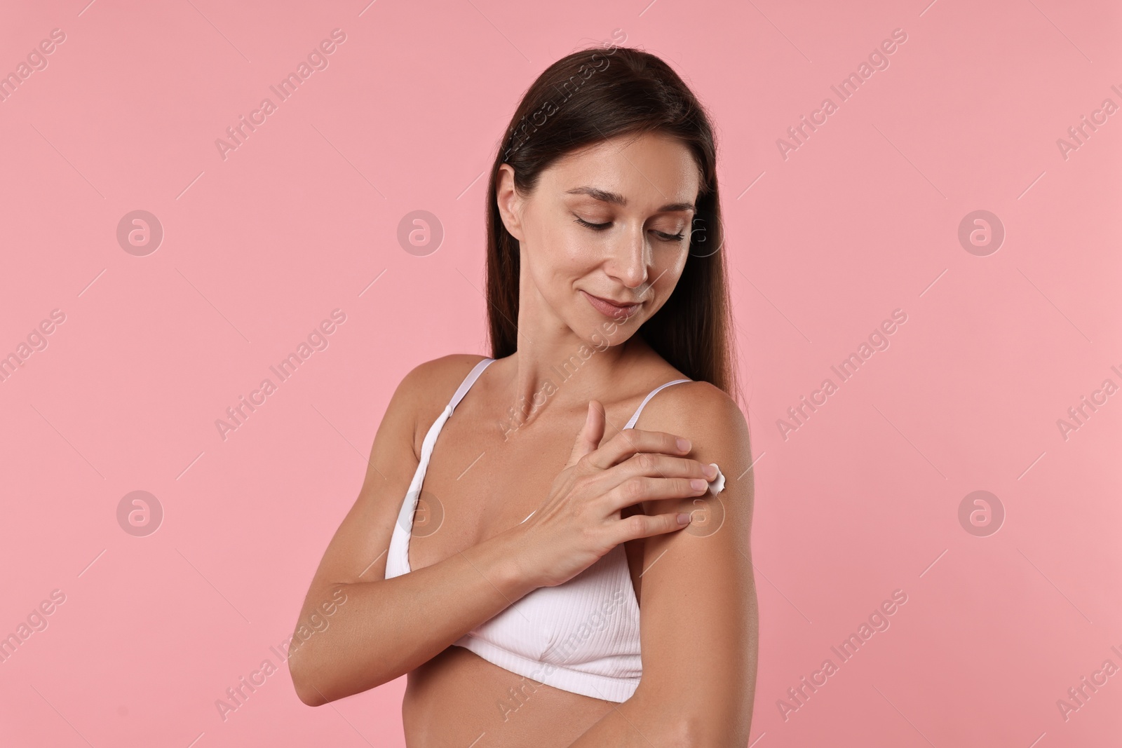 Photo of Beautiful woman applying cream onto arm on pink background. Body care