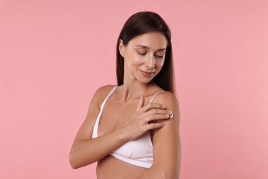 Beautiful woman applying cream onto arm on pink background. Body care