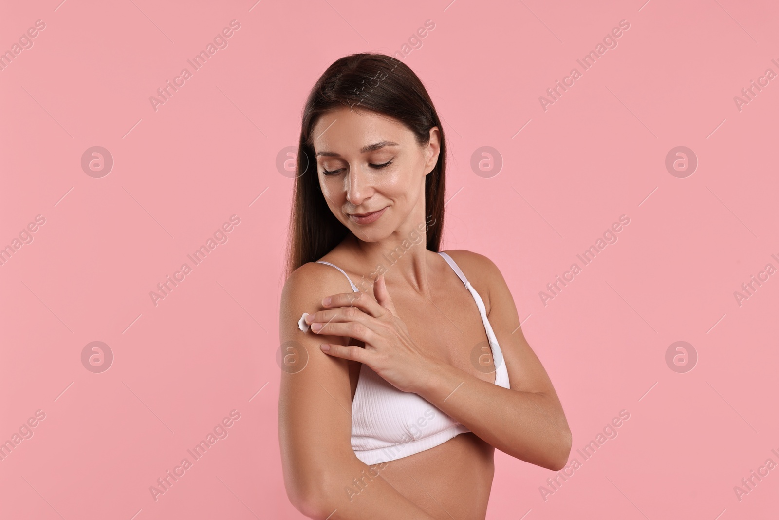 Photo of Beautiful woman applying cream onto arm on pink background. Body care