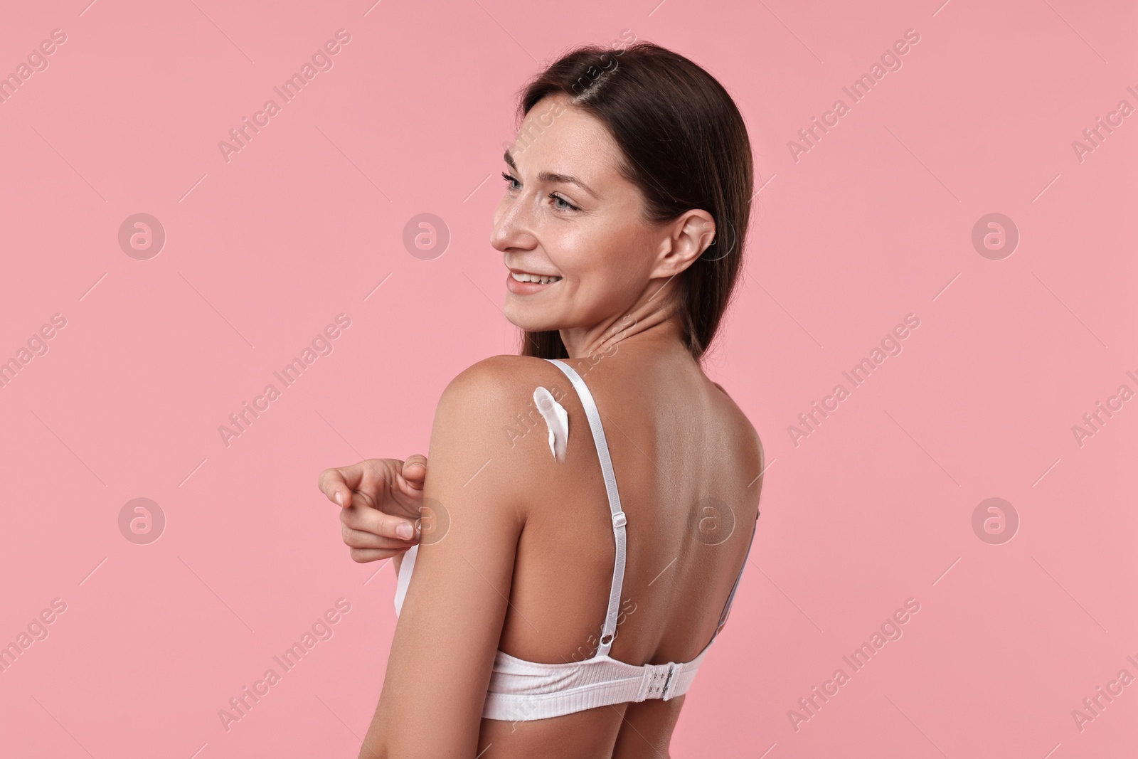 Photo of Smiling woman with cream on shoulder against pink background. Body care