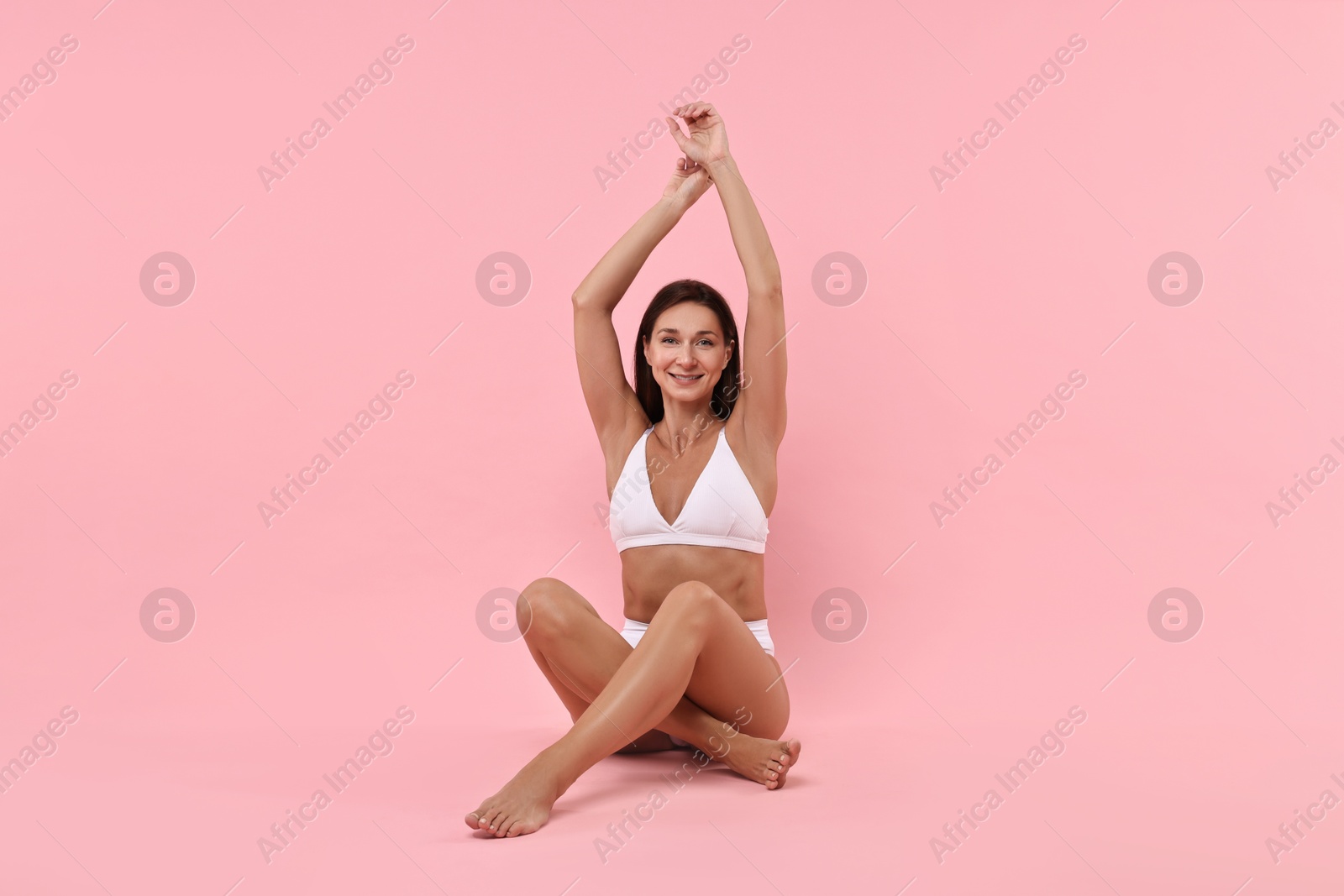 Photo of Smiling woman with perfect skin sitting on pink background. Body care