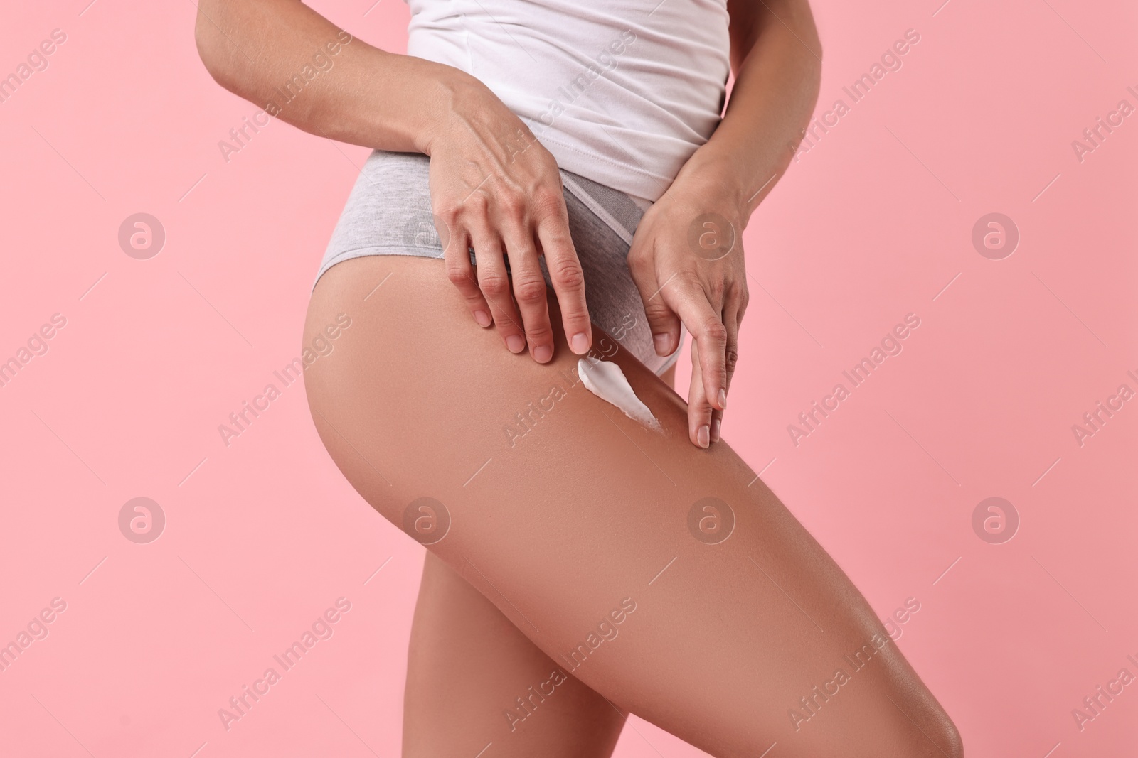 Photo of Woman applying cream onto leg against pink background, closeup. Body care