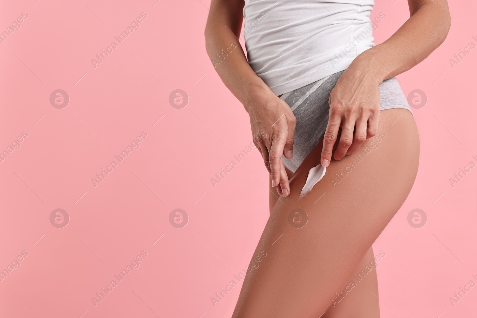 Photo of Woman applying cream onto leg against pink background, closeup with space for text. Body care